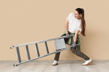 Young woman carrying heavy stepladder near beige wall