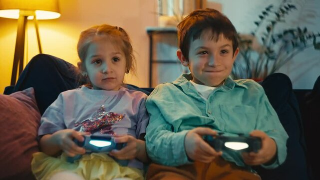 Children with joysticks in their hands playing games on TV. Brother and sister having fun together at home. High quality 4k footage