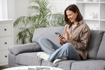 Young happy woman holding mobile phone with smart home security system control panel on sofa in room
