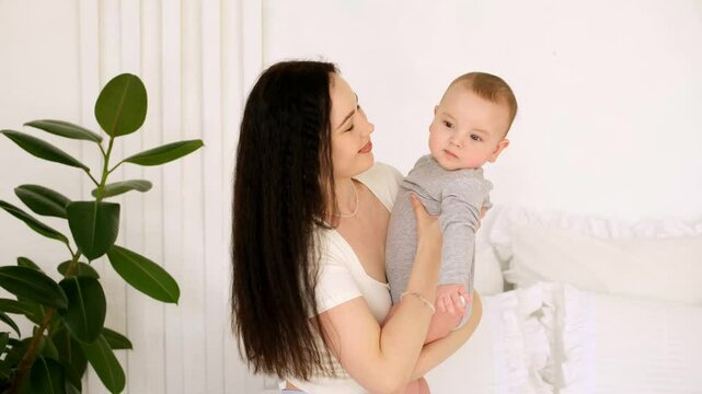 mom and baby, mother hugs and kisses baby holding him in her arms, maternal love and care, young mom having fun with baby baby, mom's decree