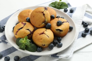 Delicious muffins with blueberries and mint on white wooden table, closeup