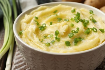 Tasty mashed potato with green onion in bowl on wooden table, closeup