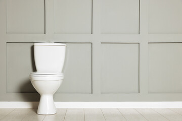 Ceramic toilet bowl near grey wall indoors