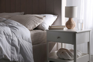 Bedside table with books, lamp and glass of water near bed in room © New Africa