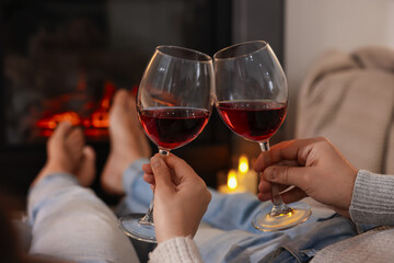 Couple with glasses of wine near fireplace at home, selective focus