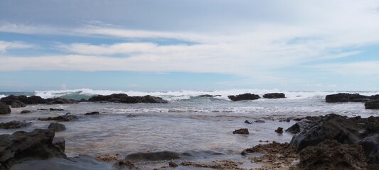 Beach with sea rocks, waves, blue sky and clouds