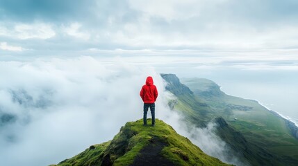 A man in a red jacket stands on a hill overlooking a body of water