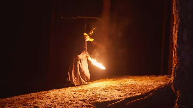 A solitary wizard walks through a dense forest at night, holding a torch that casts flickering light. He approaches the hidden location of a long-lost treasure, determined to uncover its mysteries.