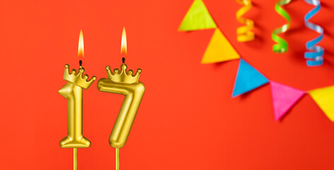 Number 17 candle - Birthday celebration on an orange background with pennants