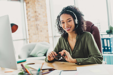 Confident young businesswoman in casual attire with headphones working in a bright modern office...