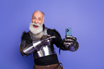 Elderly knight in full armor joyfully posing with a smartphone against a purple backdrop