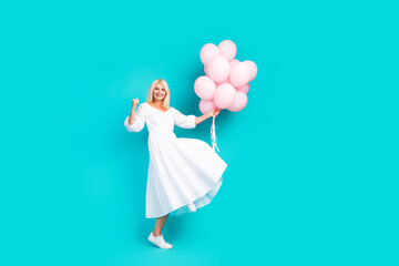 Cheerful woman in a white dress holding pink balloons against a vibrant turquoise background