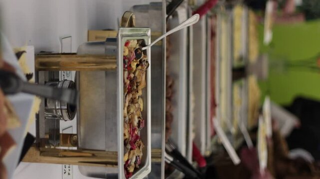 People going down two rows around a long table serving themselves food with a pasta buffet containing alfredo and marinara sauce as well as rice, vegetables and chicken.