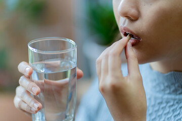 Close-up of woman taking a capsule with a glass of water, concept of health care, supplement...
