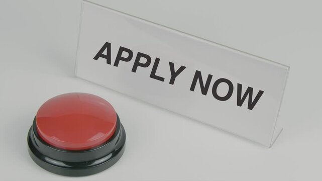 Apply Now text or word displayed on a nameplate as a hand presses a red button, symbolizing the action of applying or initiating a process, set against a white background