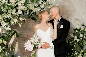 Young couple in beautiful festive outfits happily hugging and smiling near arch