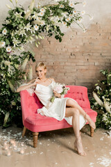 Beautiful bride with bouquet smiling in wedding dress sitting on bright pink sofa
