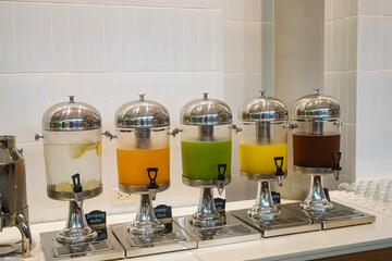 Row of stainless steel beverage dispensers with different fruit juices at a buffet breakfast station