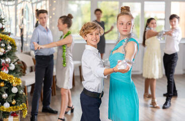 Positive teenage students in festive attire rehearsing ballroom dance number for upcoming Christmas party at college with interested female teacher in background..
