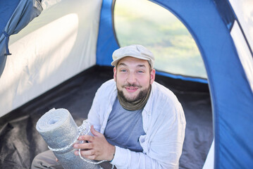 Happy traveler looking at camera and smiling broadly sitting inside his tent while camping in the...