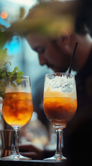 Close-up of two elegant cocktails. The bartender can be seen working in the background, blurred.