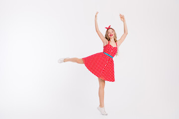 Energetic young woman in vintage polka dot dress dancing with cheerful expression on a white...