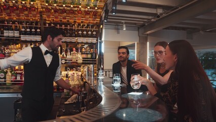 Smart bartender with VIP customer at luxurious bar greeting new beautiful guest at counter in engaging lively conversation at back view in lighting atmosphere at lighting warm nightclub. Vinosity.