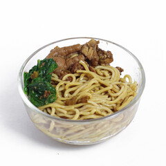 Indonesian chicken noodles (mie ayam) with chicken feet, braised chicken, and spinach in a clear bowl. Side view of traditional street food served on white background.
