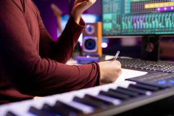 Performer writes verses and ideas to develop an original track in his home studio before recording...