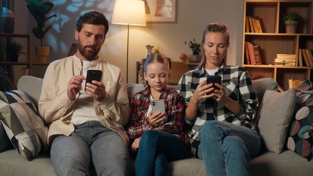 European family using mobile phones smartphones addiction dependency online internet gadgets at home in evening living room dad father yawning mother with child girl kid daughter relaxing together