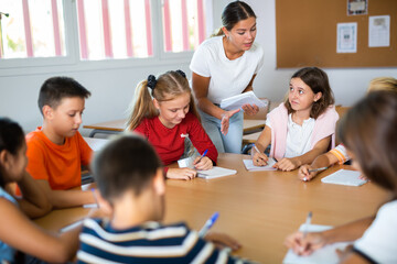 Fototapeta premium Teacher, together with group of schoolchildren, are looking for solution to complex tasck at round table in a school classroom
