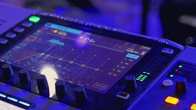 A close-up view of a professional audio mixing console, illuminated in blue. The display shows sound settings and frequency spectrum, highlighting controls for precise audio adjustment