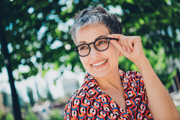 Charming mature woman with short hair wearing stylish glasses, enjoying a sunny day outdoors.