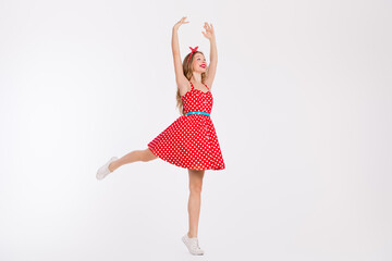 Young woman in red polka dot dress posing dynamically on white background showcasing retro fashion...