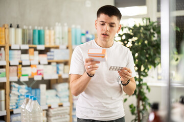 Guy is looking at the packages of medicines in the pharmacy with interest. Buyer chooses a pills...