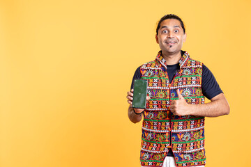 Portrait of influencer smiling and doing thumbs up gesturing presenting green screen phone, studio background. Jolly person holding chroma key smartphone, grinning and doing like sign hand gesture