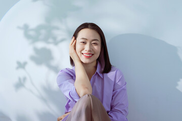 Young woman with a bright smile poses casually against a soft blue background, showcasing a relaxed...
