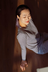 Woman in casual gray attire poses gracefully in soft light, showcasing tranquility in a cozy indoor...