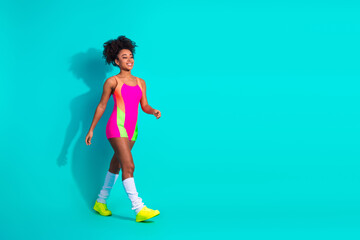 Young athletic woman in vibrant activewear walking confidently against a turquoise background...