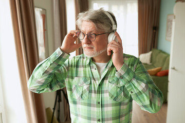 Portrait of senior man in glasses passing by room in his apartment and looking aside while...