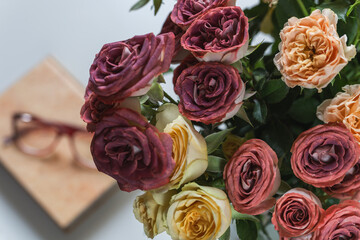 Vase with roses and a book with glasses on a white table. Selective focus.