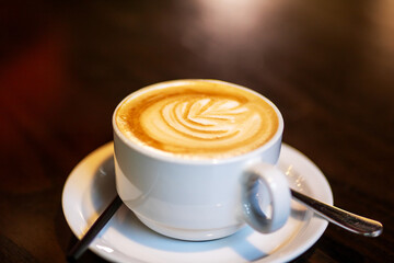 A cup of cappuccino on a saucer with a spoon