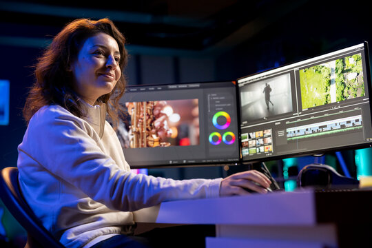 Happy videographer reviewing footage and selecting scenes, trimming them using specialized software applications and editing tools. Smiling video editor working for media company in editing room