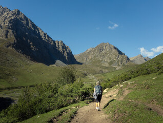 A solo female traveler walking through the scenic landscape of Tien Shan mountain range on the way...