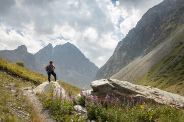 Solo female traveler standing on the rock admiring the mountain view in the scenic valley of Ala Archa National Park in Kyrgyzstan