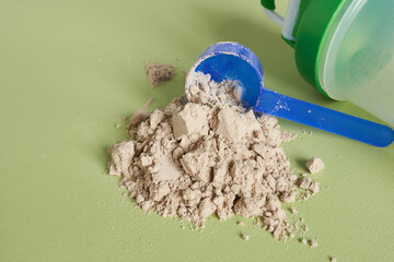 Pile of whey protein powder and scoop on green background.