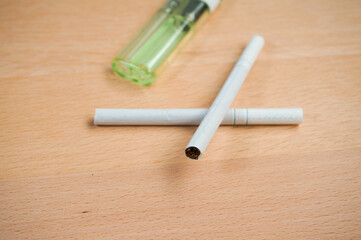 two cigarettes, white color, wooden background, lighter green color,