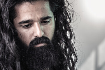 Close-up portrait of man with long, dark, wavy hair and full dark beard. contemplative expression...