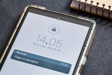 Close-up of mobile reminder Flight to Bangkok on desk. Push notifications using real-time technology concept. Vacation alert, selective focus.