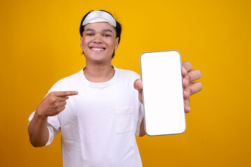Young Asian Man Wear Pyjamas and Blindfold Pointing to Smartphone Blank Screen for Mockup